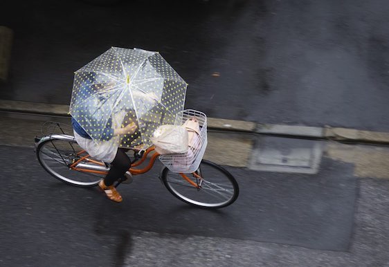 Tokyo, Japan - May 29, 2011: A Japanese woman rides her bicycle while holding an umbrella on a rainy Sunday in the Ojima area of Tokyo.