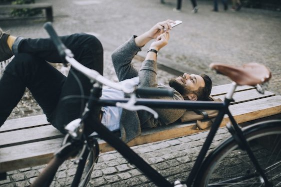 Photo of a man lying on the bench and typing on his smart phone
