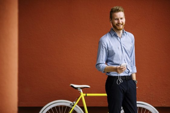 Handsome male listening music on cell phone. Bicycle on red wall