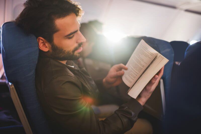 Young man traveling by airplane and reading a book.
