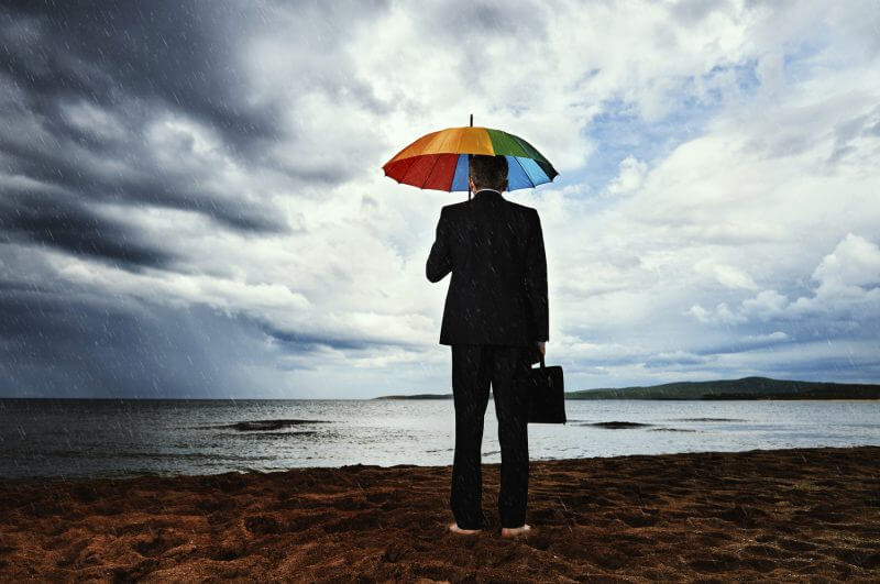 rear view of business man walking alone on the beach in stormy weather, holding briefcase and looking at the sea.