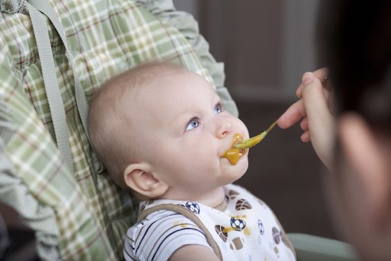 "6 month old baby boy eating solid food, looking up and not wanting to swallow."