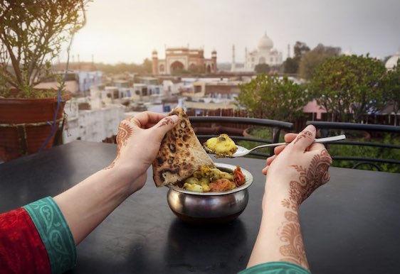Woman eating traditional Indian food in rooftop restaurant with Taj Mahal view in Agra, Uttar Pradesh, India